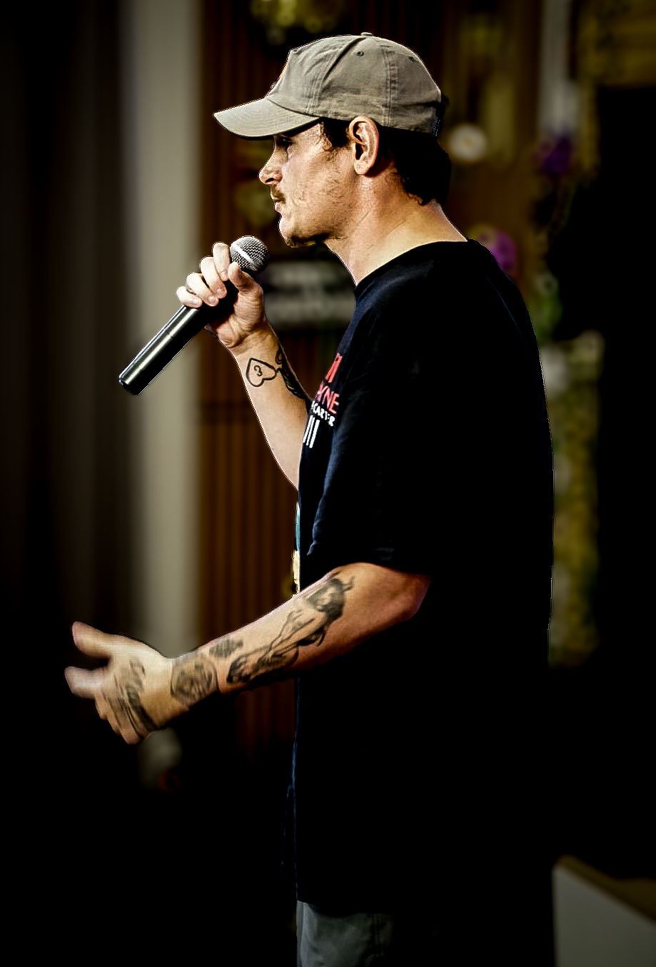 Kocain at Rhythm & Rise Live 2026, tattooed artist in black tee and tan cap singing into handheld mic in profile