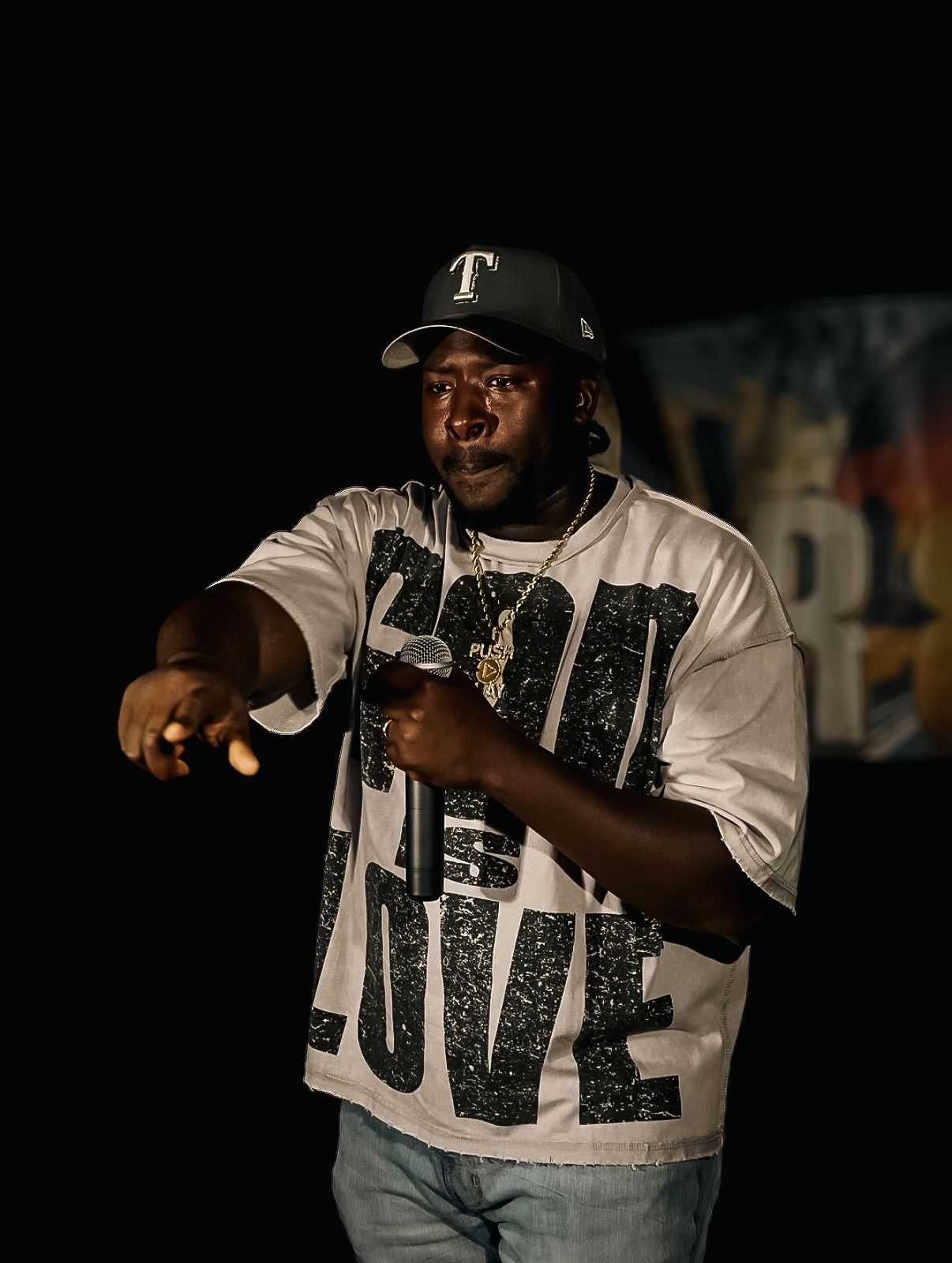 PushPlay914 at Rhythm & Rise Live 2026, in dark cap and God Is Love shirt pointing at the crowd with the mic