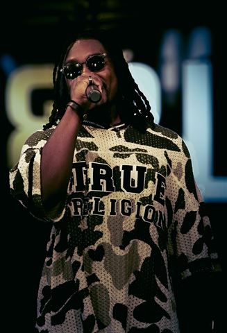 2Plby$ at RRL 2026, artist with braids and sunglasses in camo True Religion jersey rapping into handheld mic