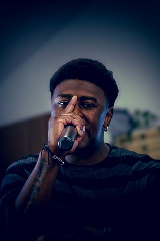 2Plby$ at RRL 2026, close-up in striped sweater rapping into mic with finger raised in cool blue light