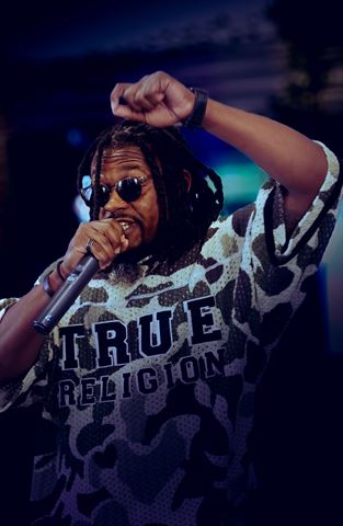 2Plby$ at RRL 2026, in sunglasses and camo True Religion jersey rapping with fist raised in blue lighting
