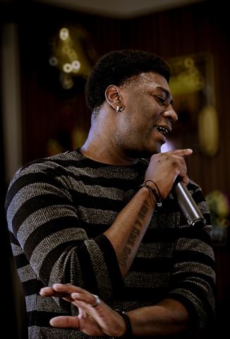2Plby$ at RRL 2026, in gray striped sweater singing into handheld mic in warm indoor lighting
