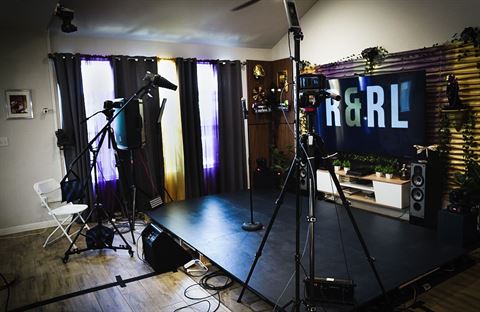 Behind the scenes at RRL 2026, the indoor stage with camera tripods, mic stand and large screen showing the R&RL logo
