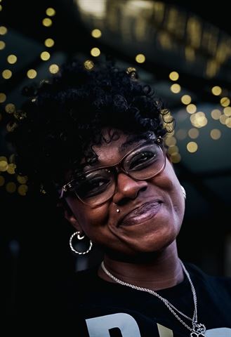 Behind the scenes at RRL 2026, smiling guest with curly hair and hoop earrings under golden string lights