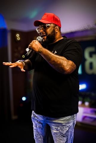 Big Tone P at RRL 2026, in red trucker cap and black tee rapping into the mic under purple lighting