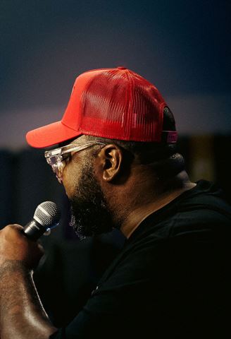Big Tone P at RRL 2026, profile in red trucker cap and glasses singing into handheld mic