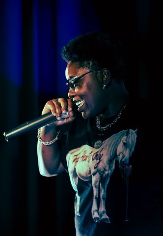 Booga Brim at RRL 2026, side profile in sunglasses and horse-graphic tee smiling into the mic in blue lighting