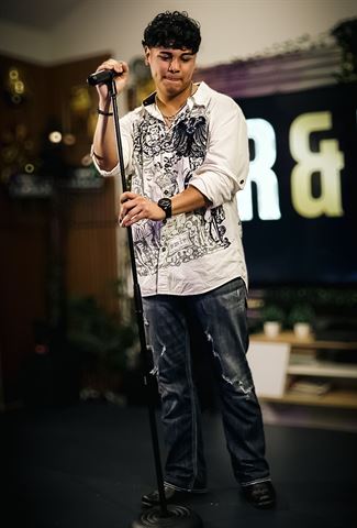 Evver The Thinker at RRL 2026, in white shirt and ripped jeans gripping the mic stand before the glowing letter sign