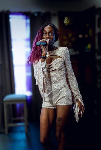 Ife Devine at RRL 2026, burgundy curls and sparkling romper, singing into the mic by the backlit window