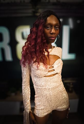 Ife Devine at RRL 2026, long burgundy waves and shimmering sequin romper before the blurred R&RL sign