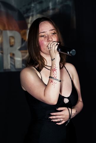 Kameryn Taelyr at RRL 2026, with red arm tattoo in black dress singing into the mic before the banner