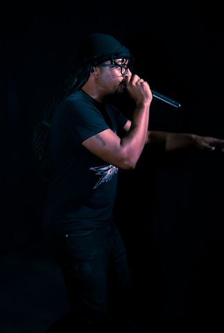 MayB.L8ter at RRL 2026, side profile rapping into mic in black durag against near-black stage backdrop