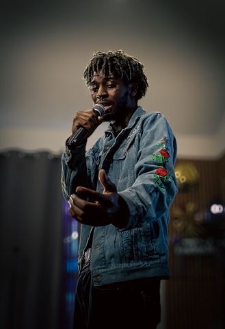 Mell. at RRL 2026, artist with dreads in rose-embroidered denim jacket singing into handheld mic