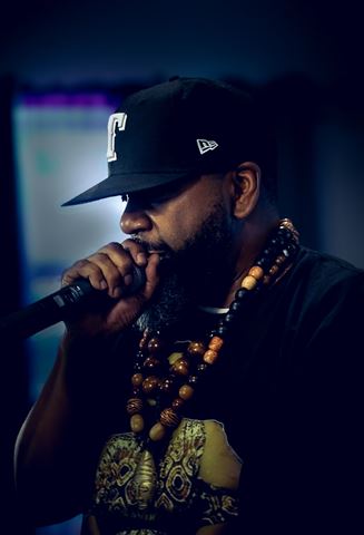 Mirage the Gr8 at RRL 2026, profile in black fitted cap with chunky bead necklaces singing into mic