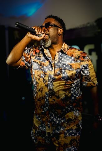 Mr Shorts, in monogram-print shirt and sunglasses rapping into handheld mic on the blue-lit stage