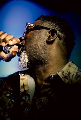 Mr Shorts, close profile in sunglasses singing into the mic under deep blue light