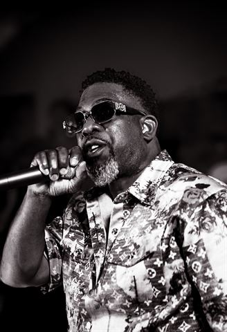 Mr Shorts, black-and-white shot in sunglasses and patterned shirt singing into the mic