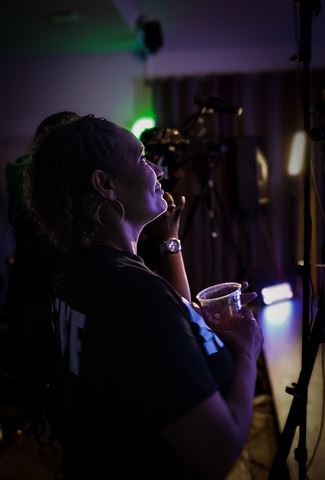 Mrs Durite, guest with hoop earrings holding a drink, watching the stage in purple light
