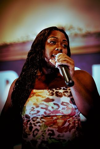 Nuu Era at RRL 2026, singing into handheld mic in floral leopard-print top under warm stage light