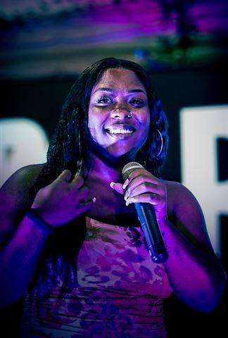 Nuu Era at RRL 2026, smiling with handheld mic in patterned dress under purple stage light