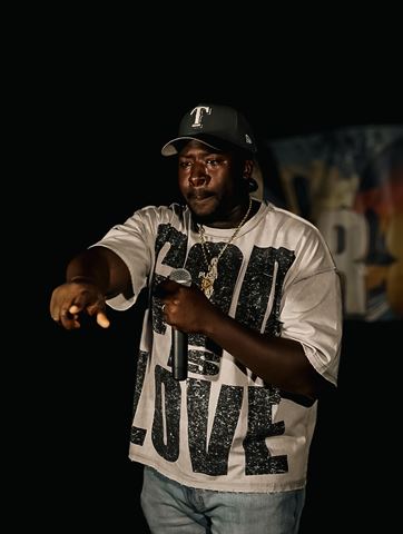 PushPlay914 at RRL 2026, in dark cap and God Is Love shirt pointing at the crowd with the mic