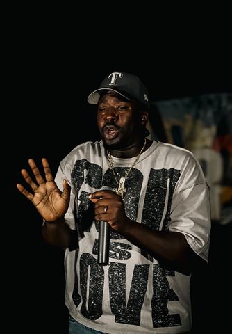 PushPlay914 at RRL 2026, in ball cap and gold chain gesturing with open palm while rapping into the mic