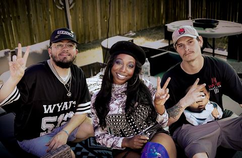 Ryan Dove DVine and Kocain at RRL 2026, three smiling people seated outdoors flashing peace signs beside a wooden fence