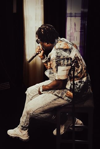 Tay No Tee at RRL 2026, in patterned shirt seated on a stool rapping into the mic against dark curtains