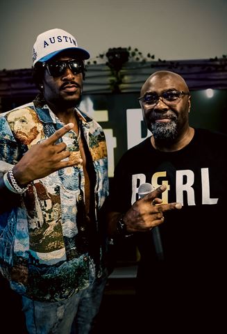 Tay No Tee and Mr Durite at RRL 2026, artist in Van Gogh print jacket posing with the host holding a mic
