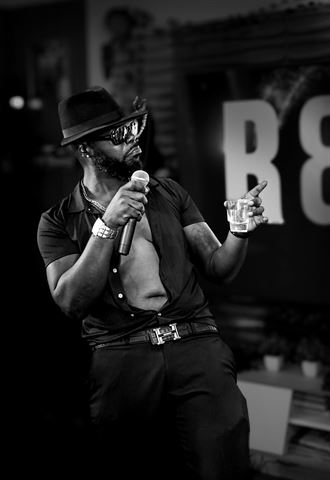 Teknition at RRL 2026, black-and-white shot in fedora and sunglasses pointing toward the stage sign