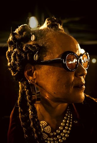 Wndy Brz at RRL 2026, profile with braided updo, cowrie shells, round sunglasses and pearls in warm light