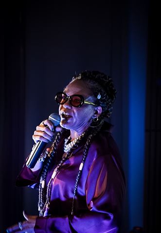 Wndy Brz at RRL 2026, in purple satin blouse and braids singing into handheld mic on the blue-lit stage