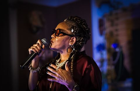 Wndy Brz at RRL 2026, in maroon top and pearls singing into handheld mic under purple-blue light