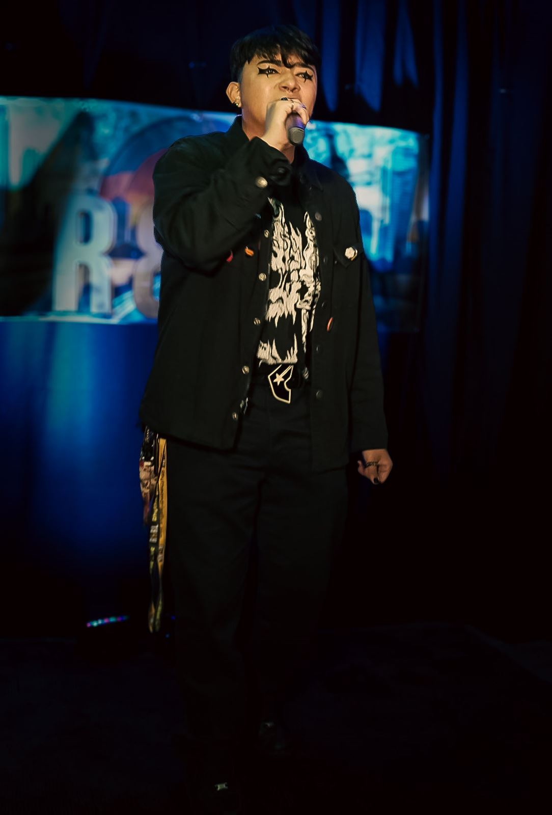 Untitled Flows at Rhythm & Rise Live 2026, in black jacket and star eye makeup singing into the mic before the blue-lit backdrop